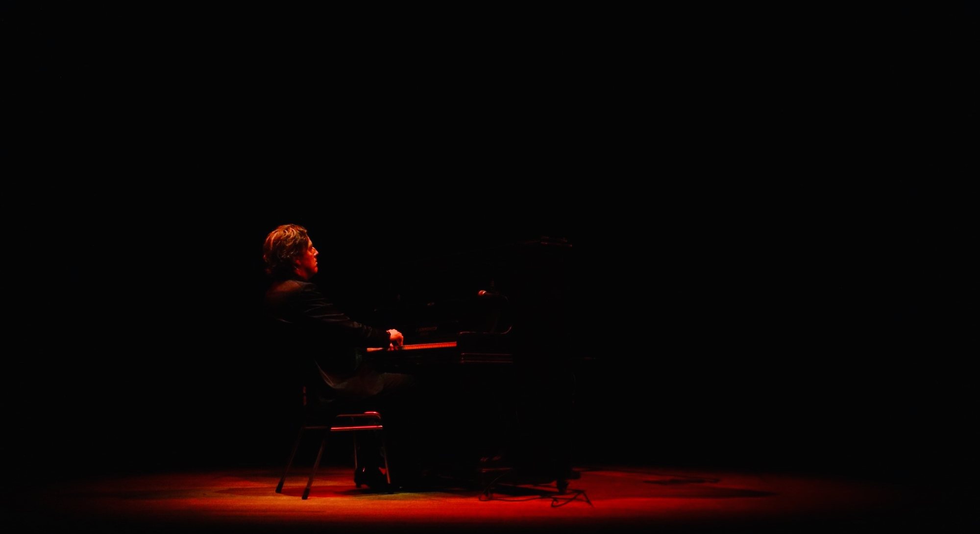 Michiel Borstlap playing solo piano in a red spotlight